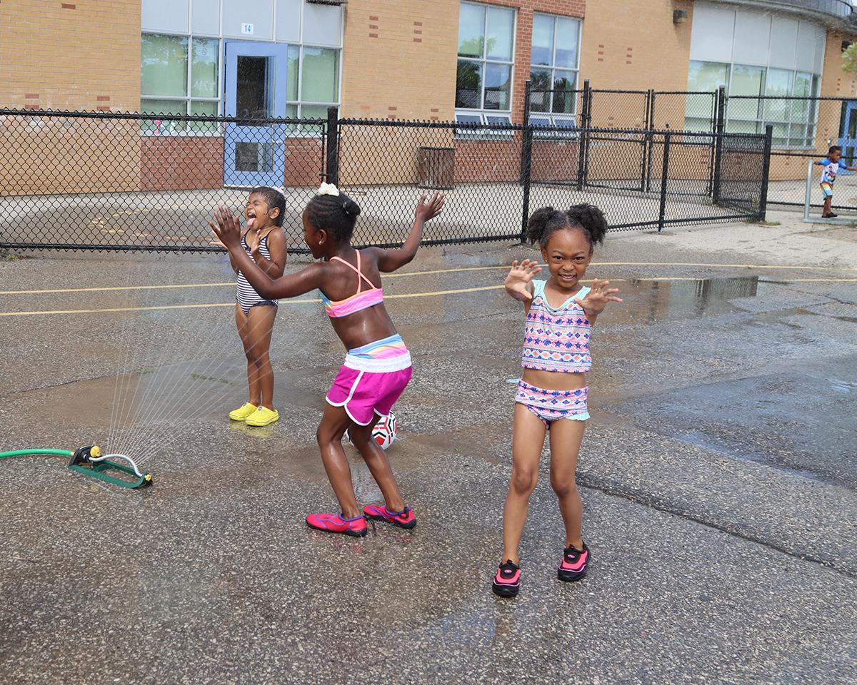 three girls having fun in a sprinkler
